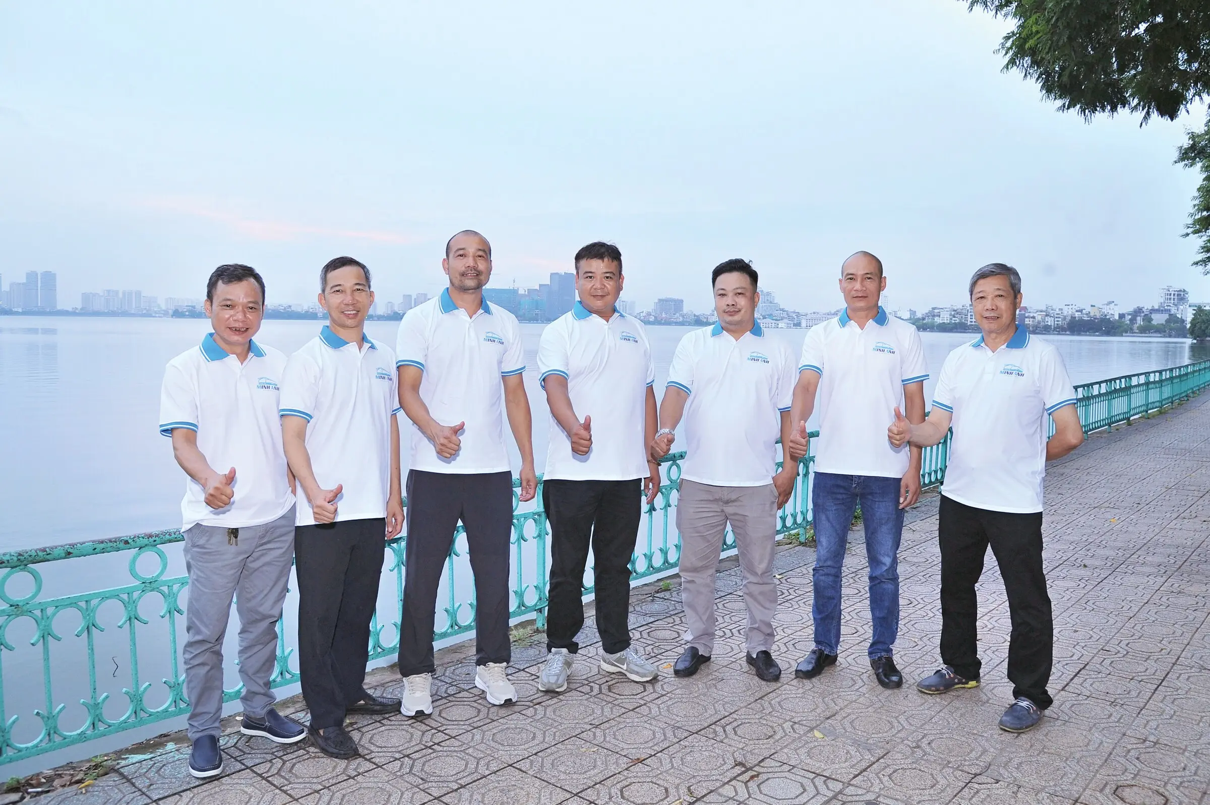 Bảy thành viên đội ngũ Minh Anh Transport mặc đồng phục bên bờ hồ