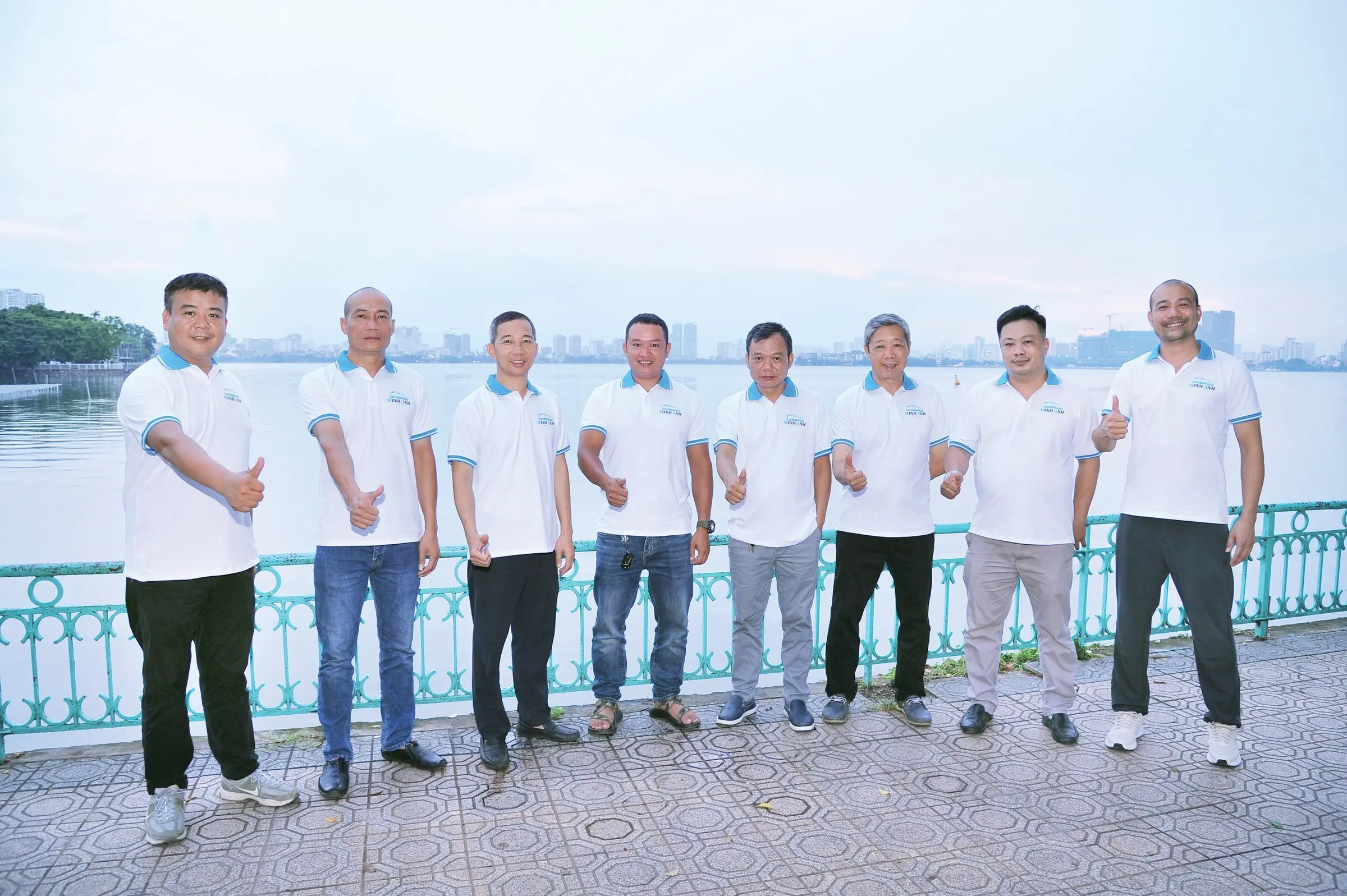 Tám thành viên đội ngũ Minh Anh Transport mặc đồng phục bên bờ hồ